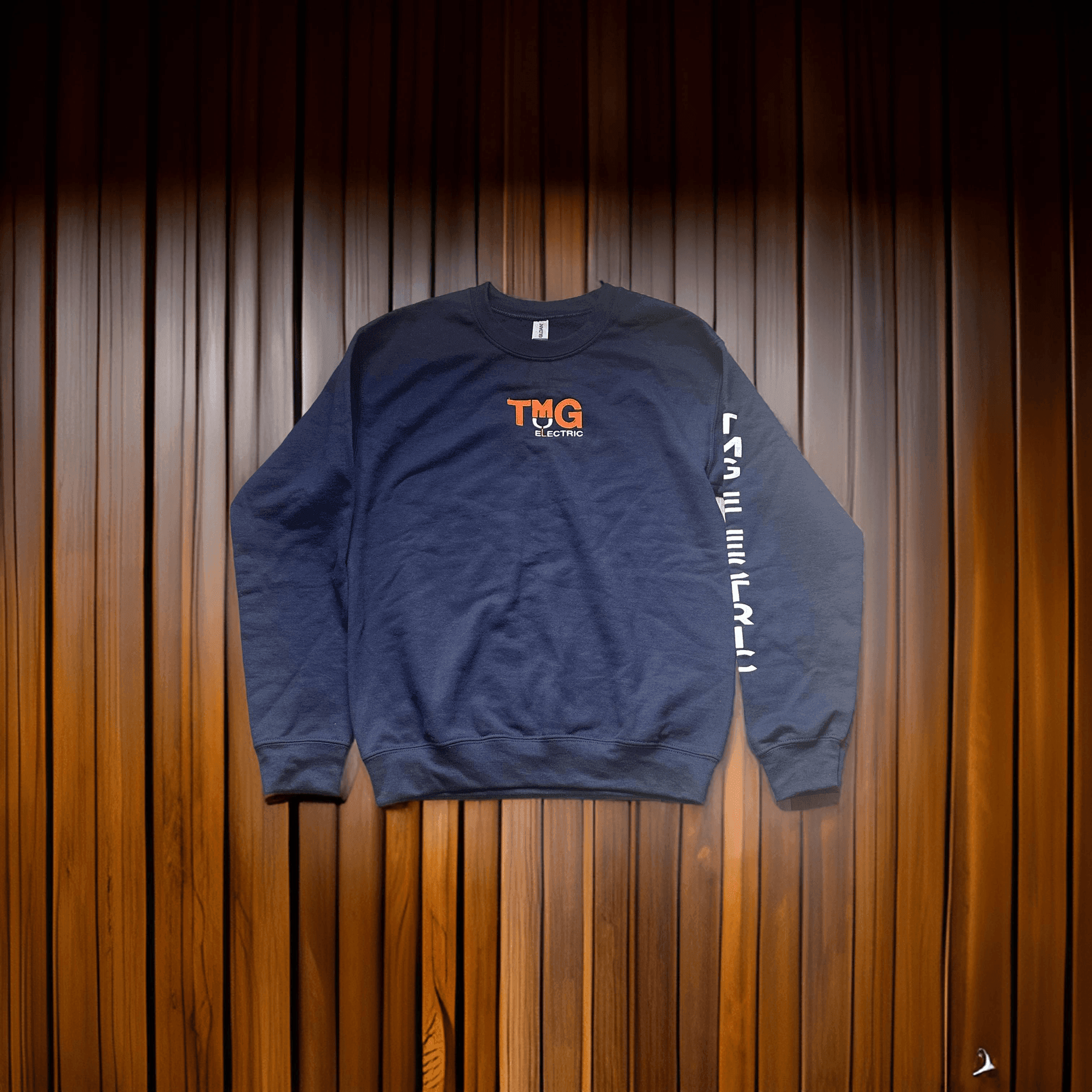 Navy blue sweatshirt with 'TMG El Electrico' logo on wooden background.