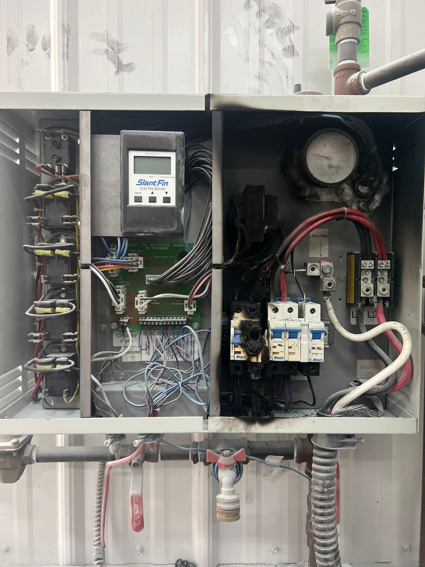 Open electrical control panel showing damaged components, wiring, circuit breakers, and a digital display screen.