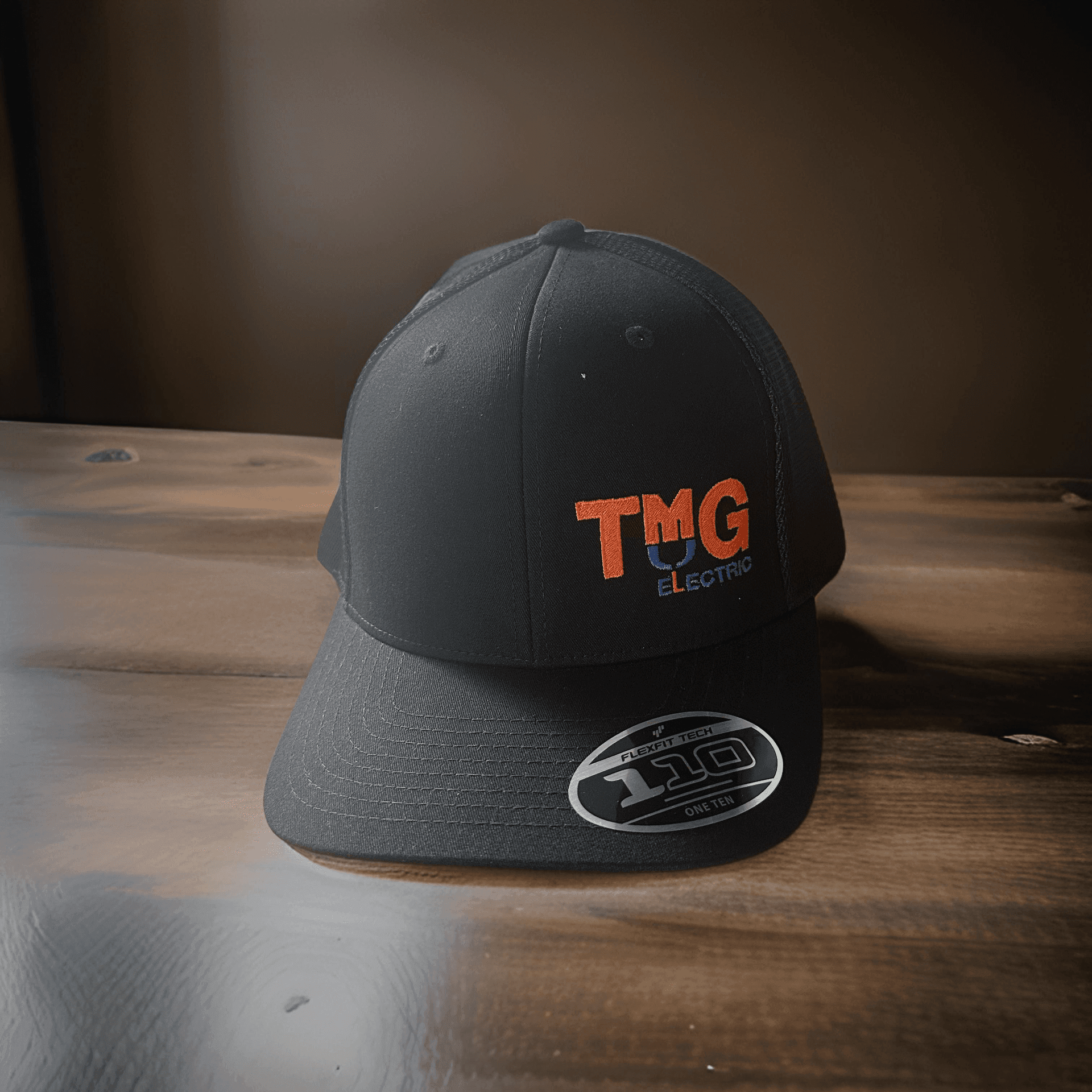 Black baseball cap with TMG Electric logo on wooden table.