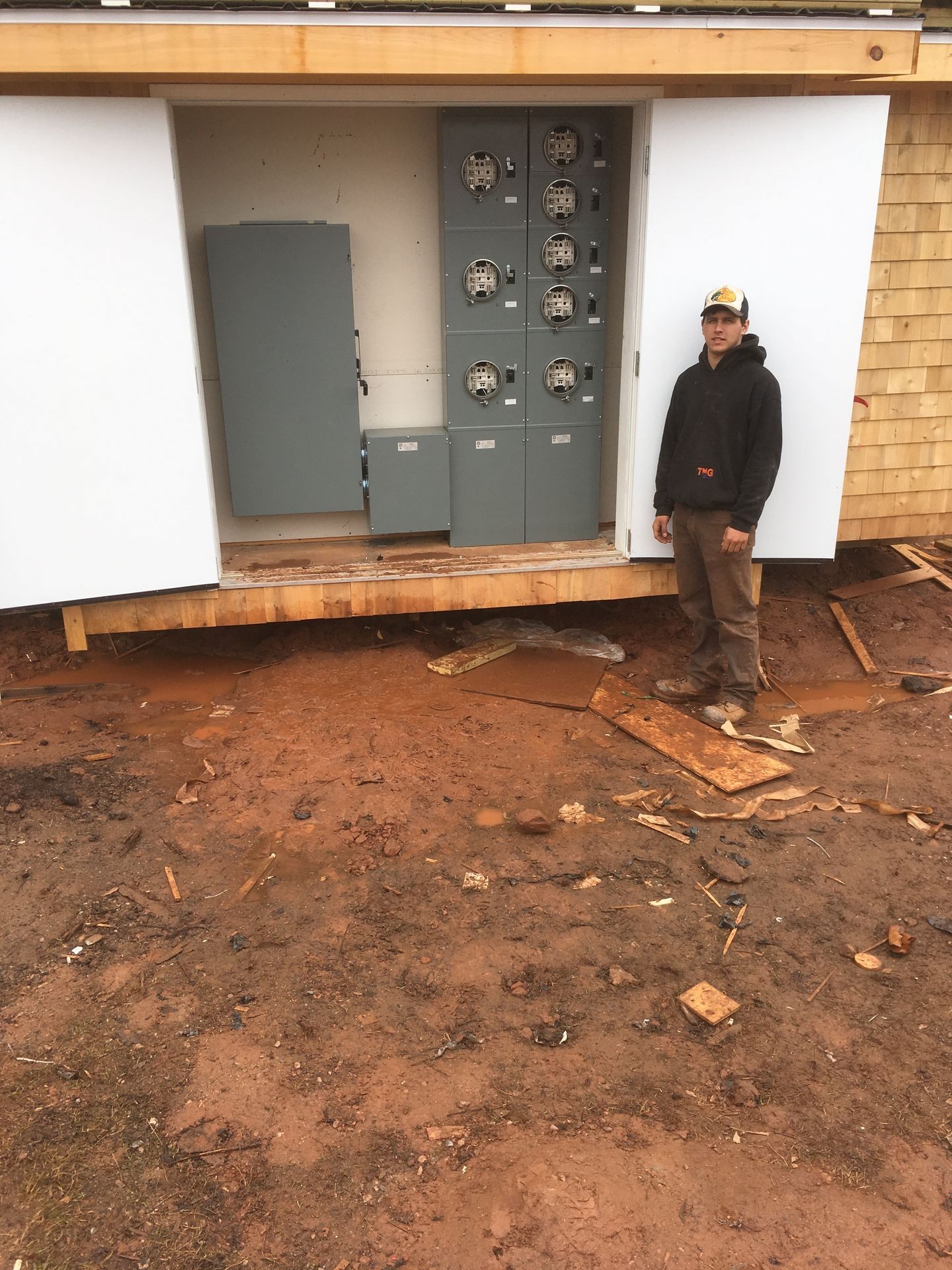 Open electrical panel with multiple meters and fuse boxes installed on a newly constructed wooden building site.